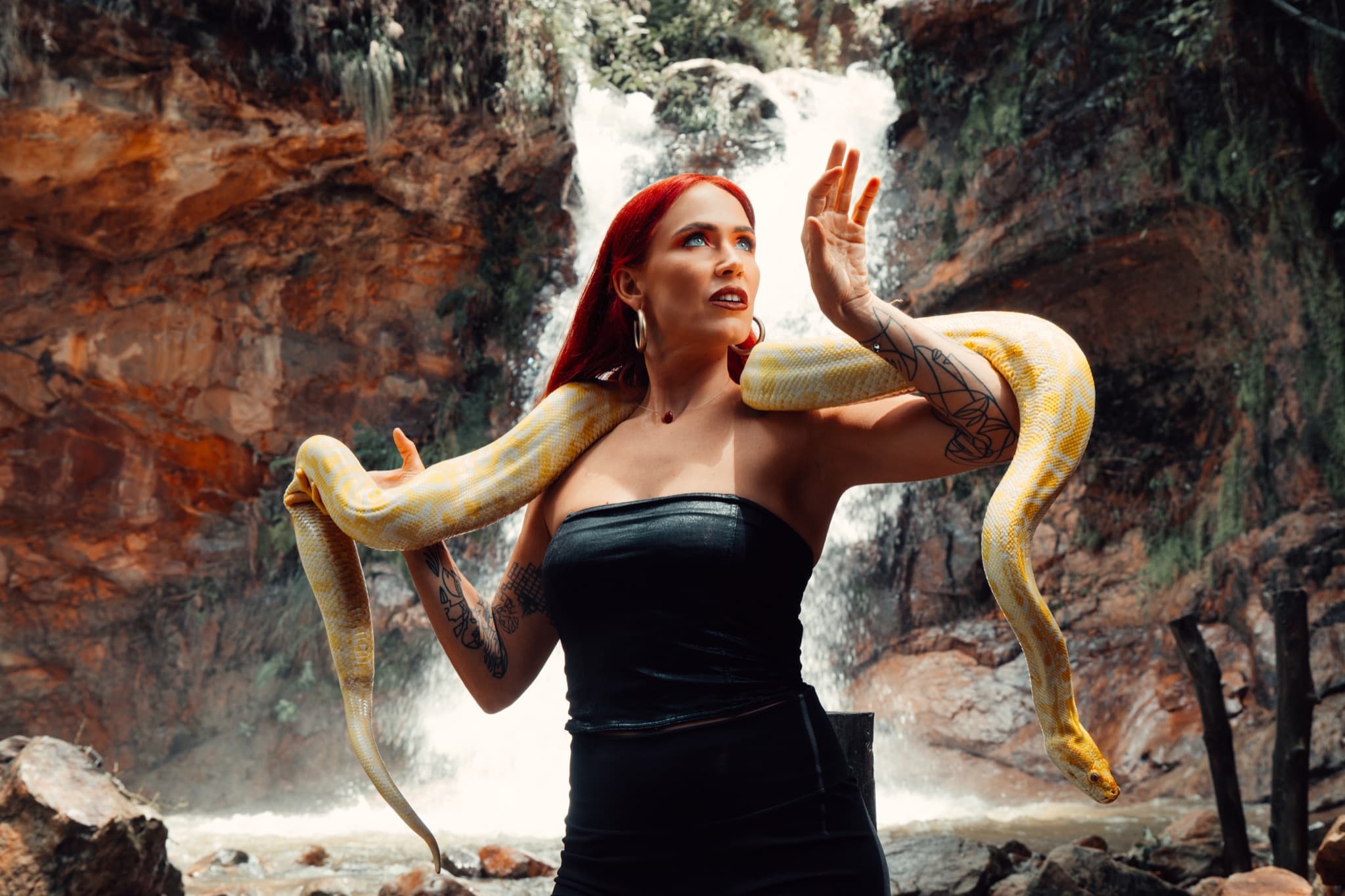 Retrato conceptual de mujer pelirroja con una pitón amarilla frente a una cascada
