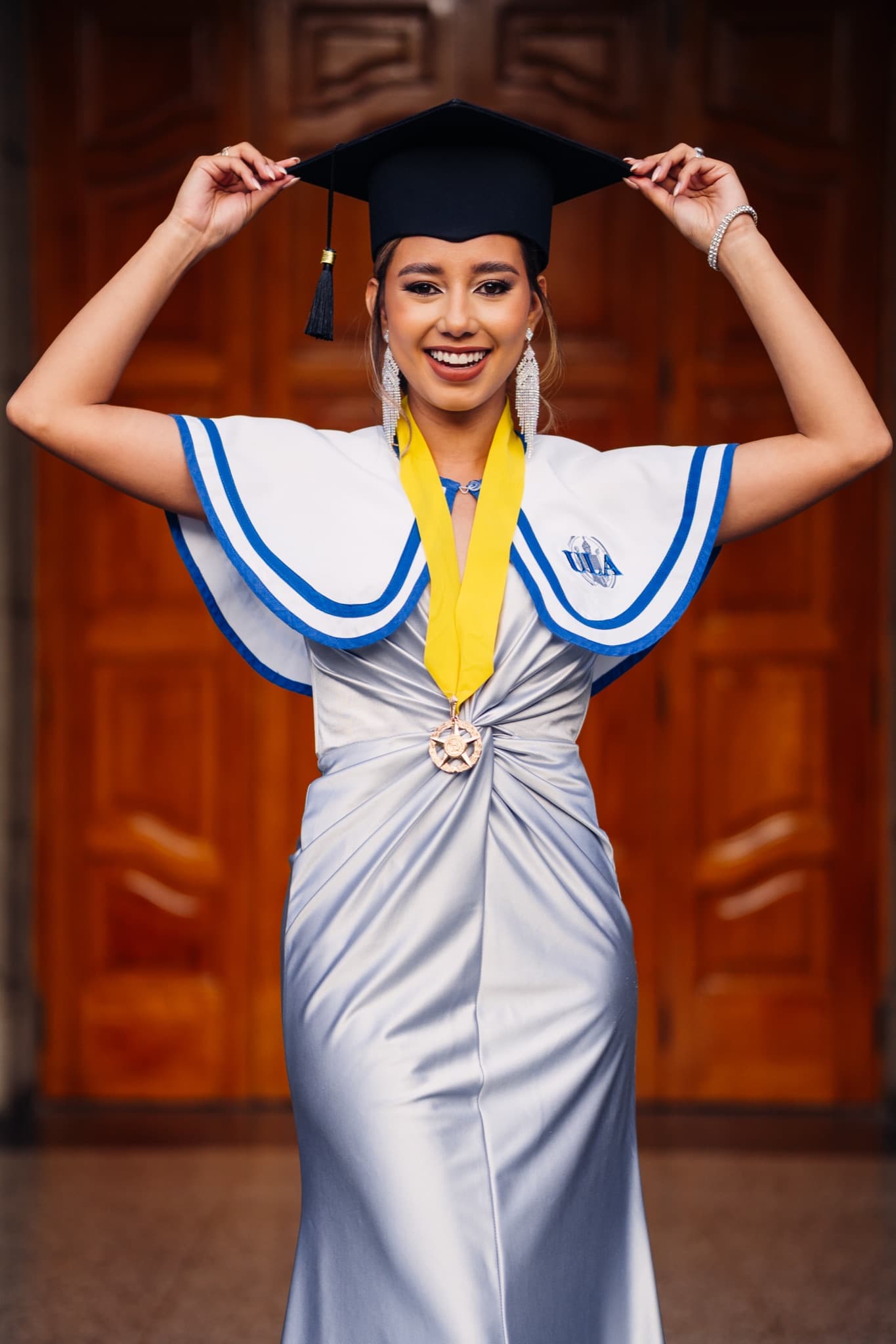 Graduada con vestido plateado celebrando con su birrete