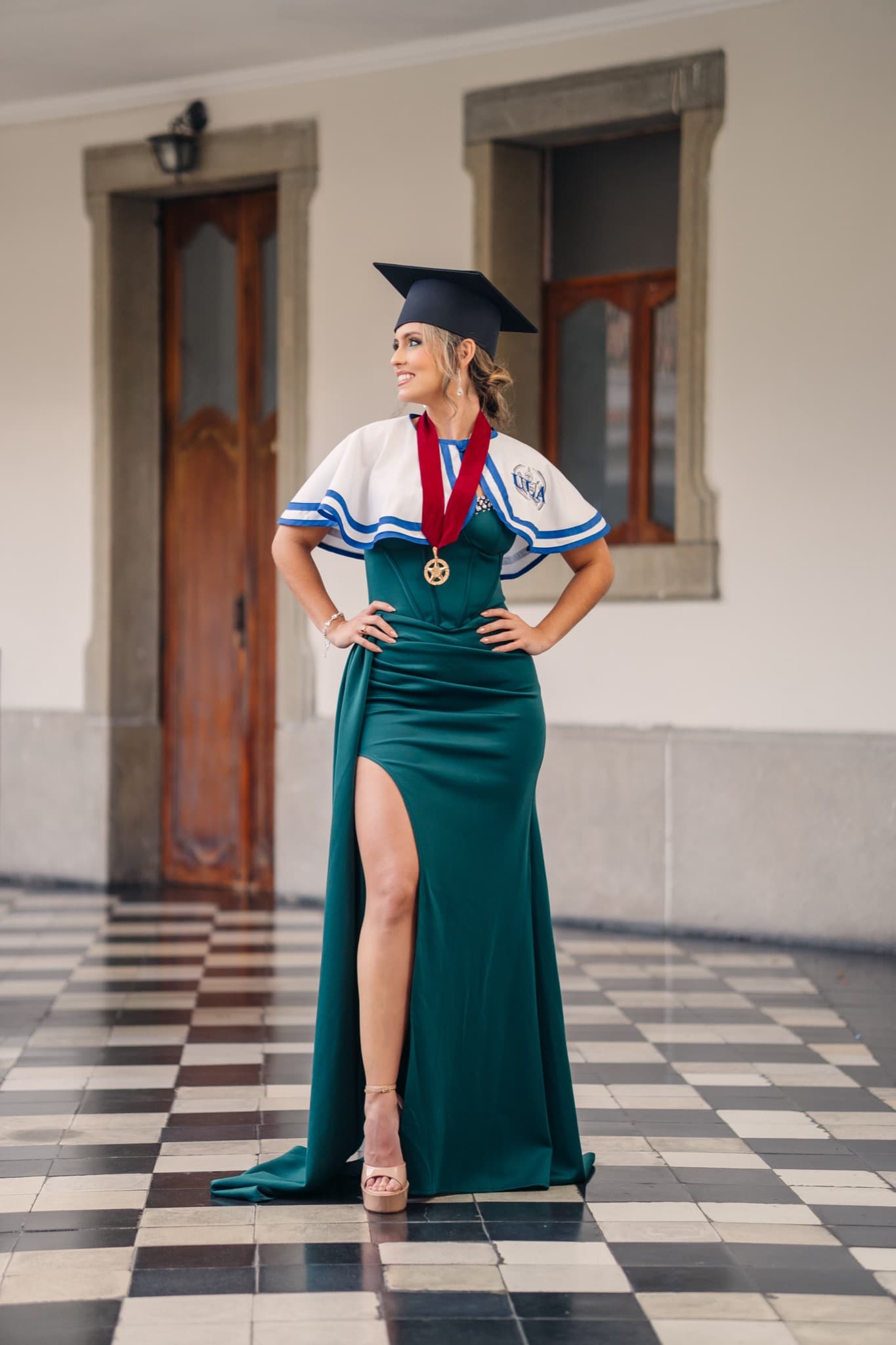 Graduada con vestido verde, capa y medalla en pose de cuerpo completo